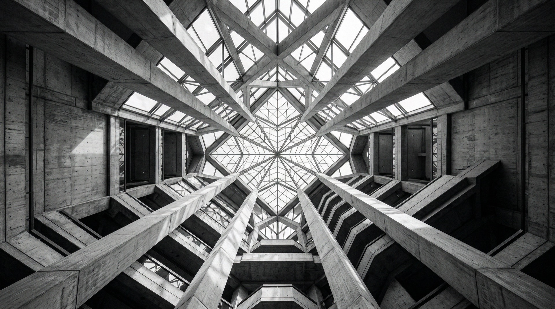 Looking upward inside a grand modernist atrium with soaring concrete columns and geometric glass ceiling